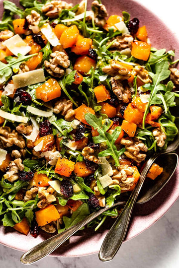 Salad with arugula, butternut squash, walnuts, and dried cranberries on a pink plate.